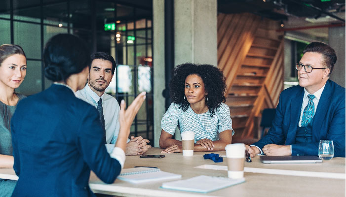 A group of co-workers sit a table and talk business while drinking coffee