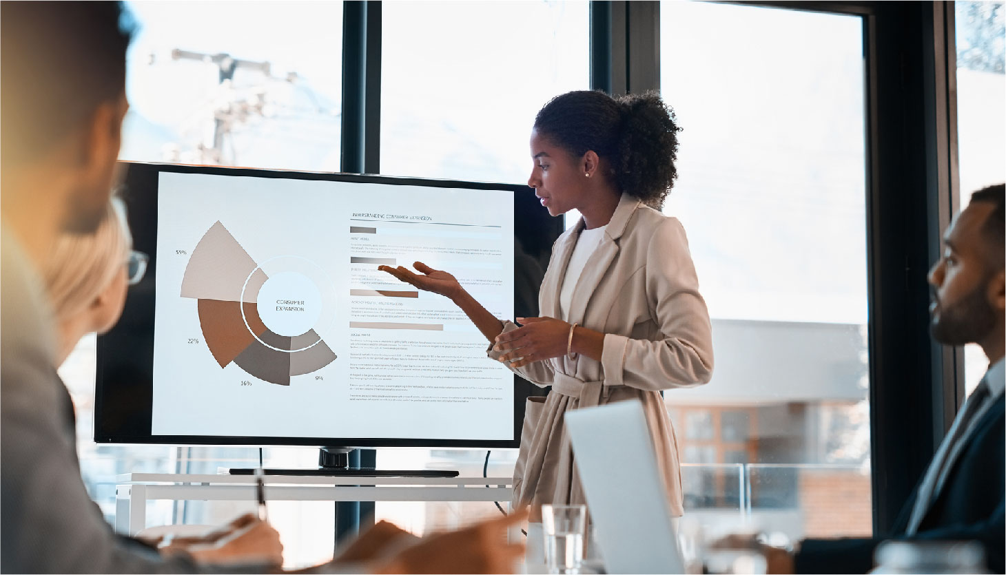 A woman points at a monitor and shows her colleagues graphs and other data