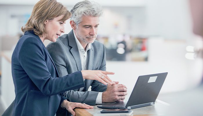 A man and a woman talk and look at a laptop screen in the office