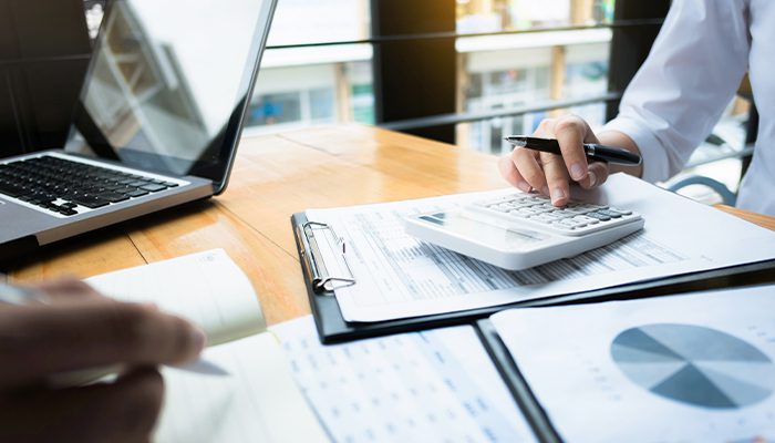 A person working at an office desk with a calculator and clipboard