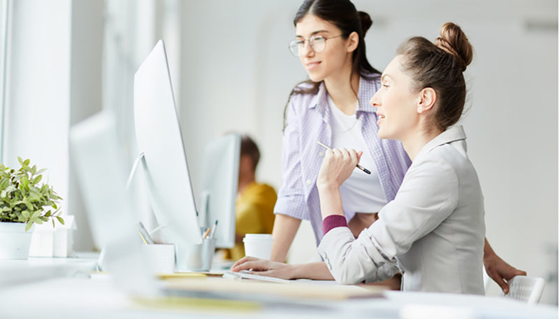 Two women work together at the office and look at a computer screen