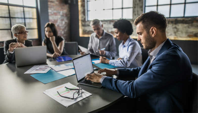 A group of coworkers sit at a desk and work on their laptops