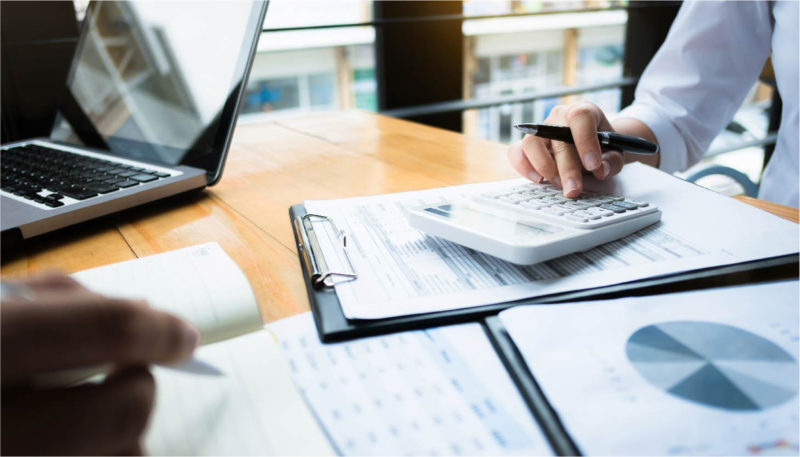 An office worker sits at his desk and uses a calculator while looking at charts