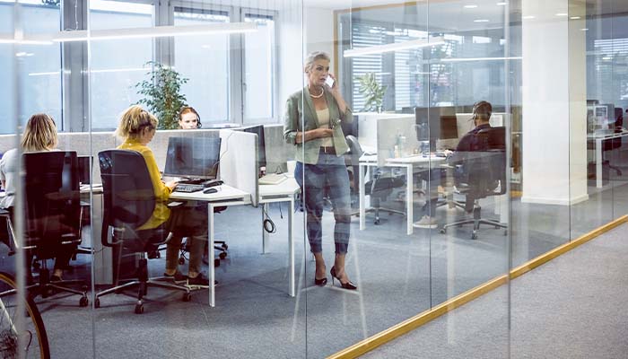 A woman in the office talking on her phone while standing next to cubicles