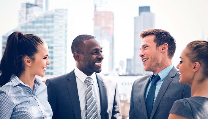 Four professionals smile and talk with one another outside the office