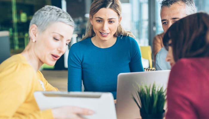 A woman shows three other coworkers her laptop screen at the office